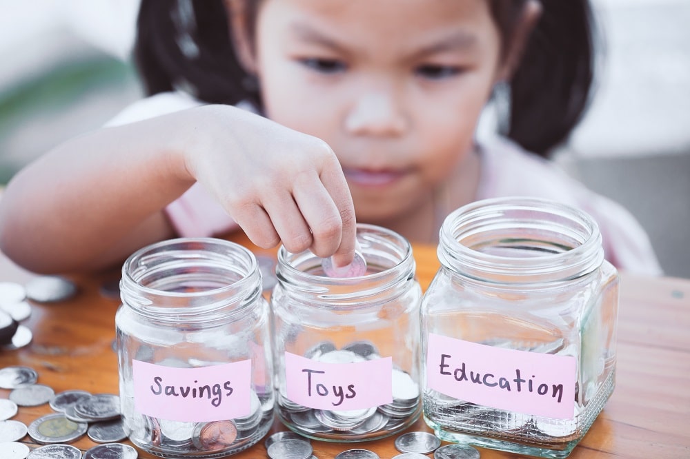Little girl with three jars of money applies saving and spending milestones for kids by age to her saving method